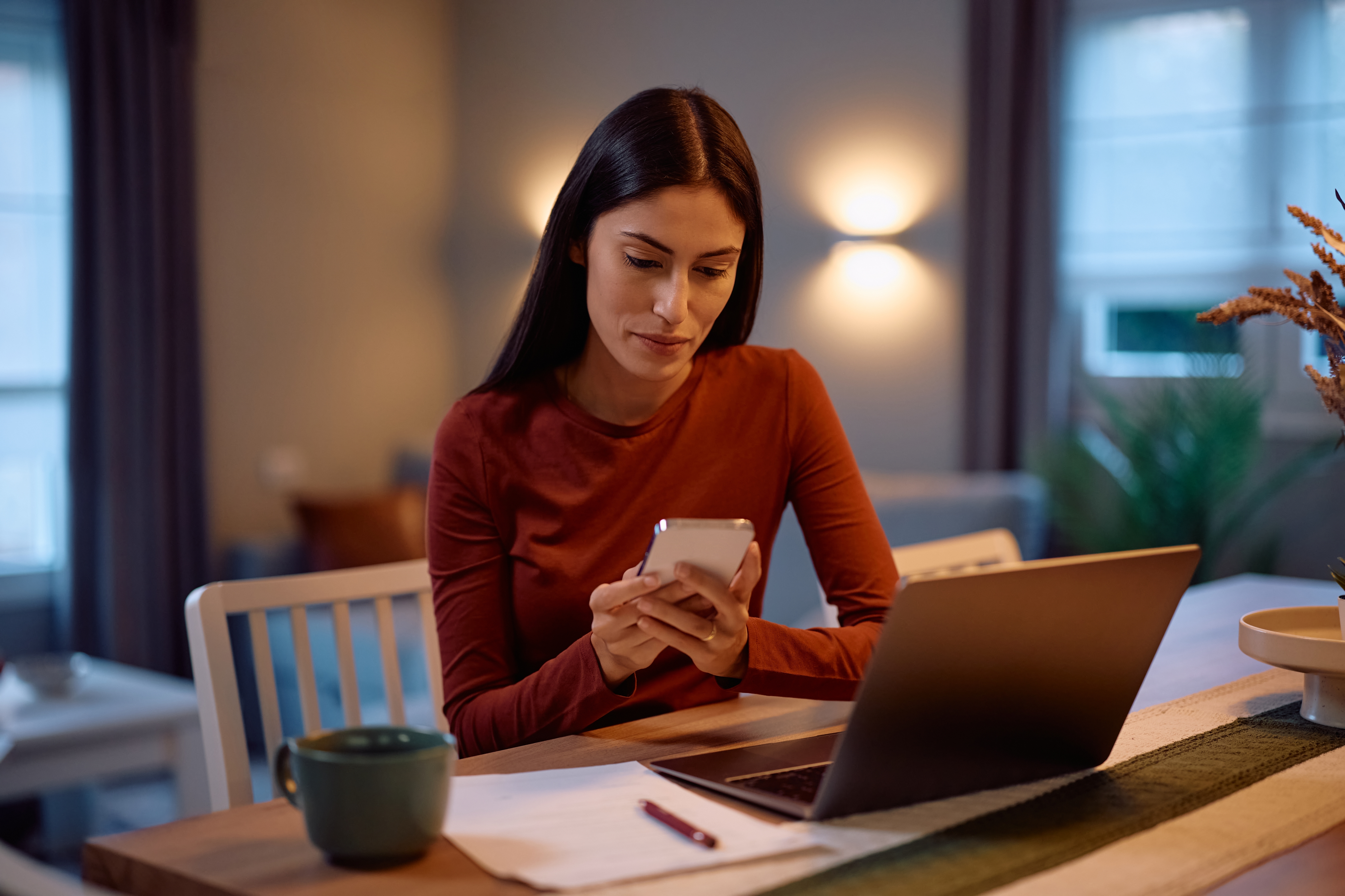 A woman using a smartphone and laptop at home, demonstrating a fast and reliable home wifi connection.